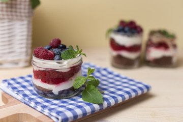 Raspberry cakes in glass jar with fresh fruit and cream cheese on a blue napkin.