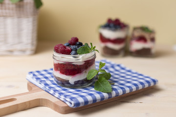 Raspberry cakes in glass jar with fresh fruit and cream cheese on a blue napkin.