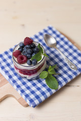 Raspberry cakes in glass jar with fresh fruit and cream cheese on a blue napkin.