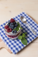 Raspberry cakes in glass jar with fresh fruit and cream cheese on a blue napkin.