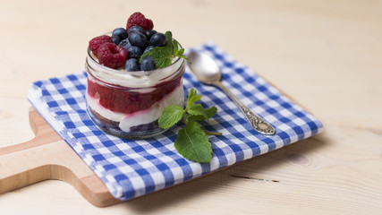Raspberry cakes in glass jar with fresh fruit and cream cheese on a blue napkin.
