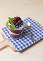 Raspberry cakes in glass jar with fresh fruit and cream cheese on a blue napkin.