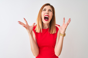 Redhead businesswoman wearing elegant red dress standing over isolated white background crazy and mad shouting and yelling with aggressive expression and arms raised. Frustration concept.