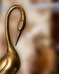 Abstract Bronze Crane metal Heron with bend neck against blurry brown background. Vintage Art.