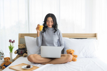 Asian woman sitting and using laptop in bedroom. .