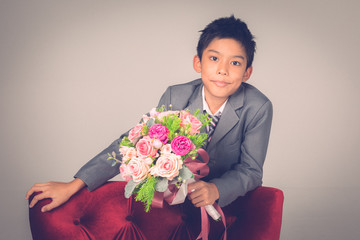 Boy in suit standing and holding a bouquet..