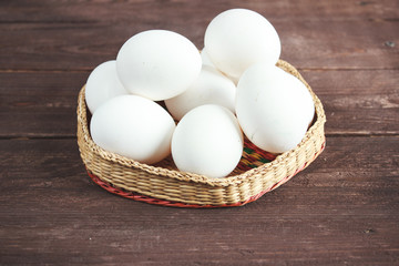 White chicken eggs in a wicker bowl on a dark wooden background