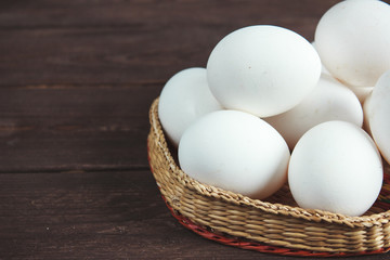 White chicken eggs in a wicker bowl on a dark wooden background