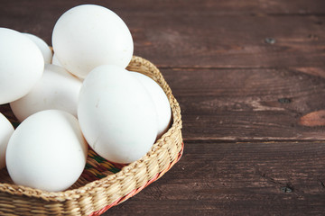 White chicken eggs in a wicker bowl on a dark wooden background