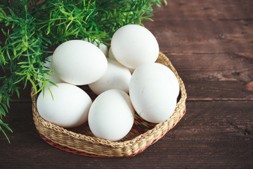 White chicken eggs in a wicker bowl on a dark wooden background