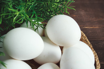 White chicken eggs in a wicker bowl on a dark wooden background