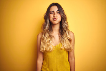 Obraz premium Young beautiful woman wearing t-shirt over yellow isolated background puffing cheeks with funny face. Mouth inflated with air, crazy expression.
