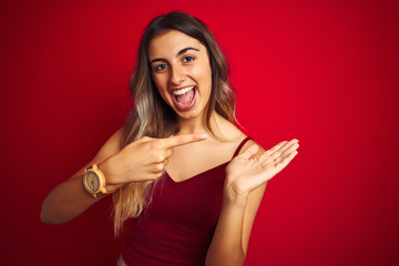 Young beautiful woman wearing a t-shirt over red isolated background amazed and smiling to the camera while presenting with hand and pointing with finger.