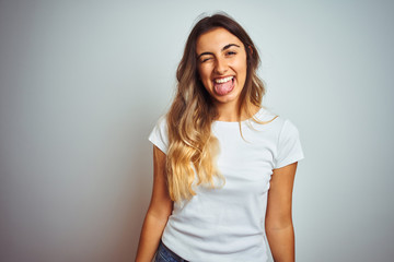 Obraz premium Young beautiful woman wearing casual white t-shirt over isolated background sticking tongue out happy with funny expression. Emotion concept.