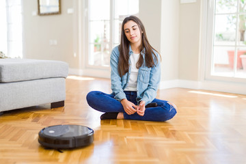 Young woman using automatic vacuum cleaner to clean the floor, controling machine housework robot