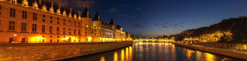 Obraz na płótnie Canvas Panorama of Illuminated Conciergerie and Pont Neuf bridge at night - Paris, France.