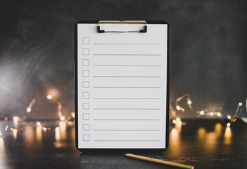 clipboard with blank list with cases to tick off on wooden desk with string lights bokeh in the background