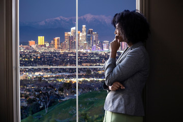 Black female business woman looking out the window of an office in Los Angeles.  She looks like a...