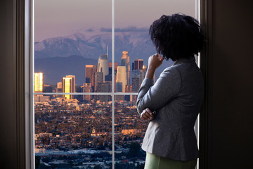 Black female business woman looking out the window of an office in Los Angeles.  She looks like a...