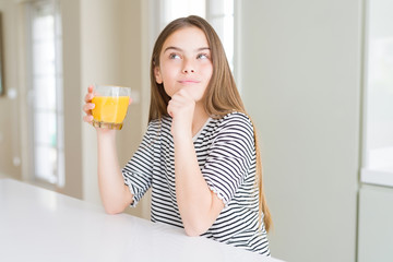 Beautiful young girl kid drinking a glass of fresh orange juice serious face thinking about question, very confused idea