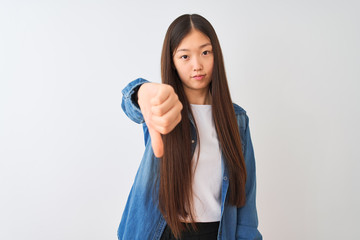 Young chinese woman wearing denim shirt standing over isolated white background looking unhappy and angry showing rejection and negative with thumbs down gesture. Bad expression.