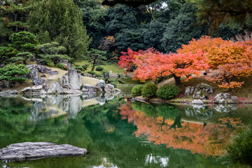 Amazing red and orange fall leaves on the right side with smooth gray stone on the left, trees in the background and deep green water reflecting all of it