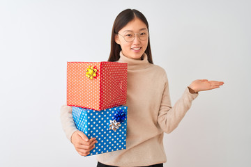 Young chinese woman holding birthday gifts over isolated white background smiling cheerful presenting and pointing with palm of hand looking at the camera.