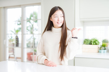 Beautiful Asian woman wearing casual sweater smiling with happy face looking and pointing to the side with thumb up.