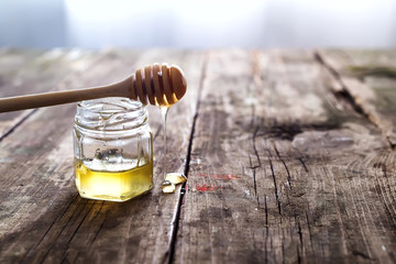 Honey dripping from a wooden honey dipper in a jar on wooden grey rustic background