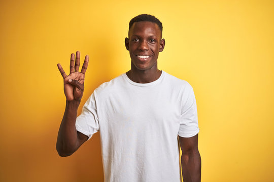 Young african american man wearing white t-shirt standing over isolated yellow background showing and pointing up with fingers number four while smiling confident and happy.