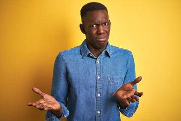 Young african american man wearing denim shirt standing over isolated yellow background clueless...
