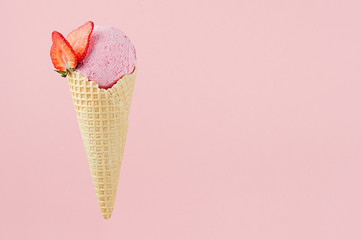 Pink creamy ice cream in crisp waffle cone with strawberry slices on pastel pink background, copy space.