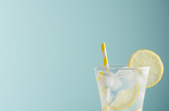 Bright cold transparent lemon cocktail with citrus slice, sparkling water, ice cubes, straw in misted glass in mint background, top, closeup, edge, half.
