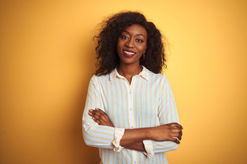 African american woman wearing striped shirt standing over isolated yellow background happy face smiling with crossed arms looking at the camera. Positive person.