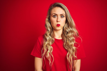 Young beautiful woman wearing basic t-shirt standing over red isolated background puffing cheeks with funny face. Mouth inflated with air, crazy expression.