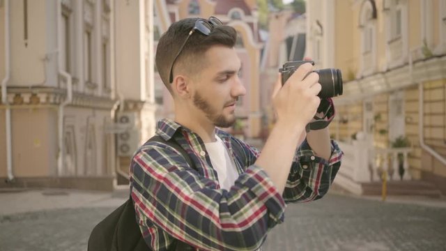 Young newbie bearded photographer taking a photo in the street of an old city with beautiful architecture. Tourist takes picture of cityscape. Photography and tourism concept. Profession, creativity