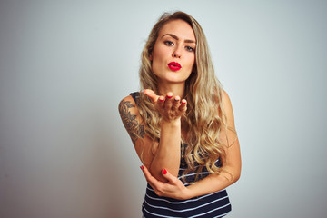 Young beautiful woman wearing stripes t-shirt standing over white isolated background looking at the camera blowing a kiss with hand on air being lovely and sexy. Love expression.
