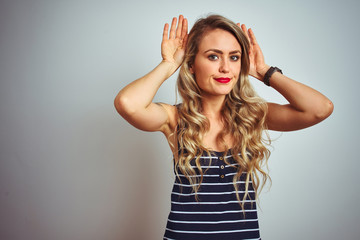 Fototapeta premium Young beautiful woman wearing stripes t-shirt standing over white isolated background Doing bunny ears gesture with hands palms looking cynical and skeptical. Easter rabbit concept.