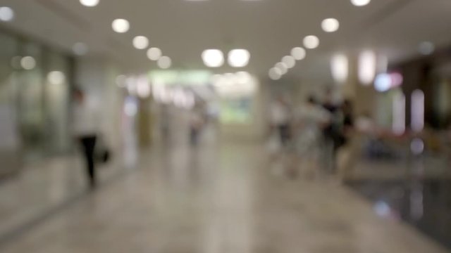 Defocused view of a bright wide hallway in a modern office building. Glass walls of meeting rooms, people walking in the corridor. Intentional blur.