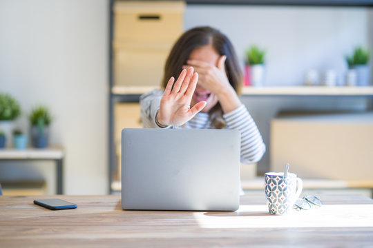 Middle age senior woman sitting at the table at home working using computer laptop covering eyes with hands and doing stop gesture with sad and fear expression. Embarrassed and negative concept.