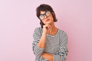 Young beautiful woman wearing striped t-shirt and glasses over isolated pink background with hand on chin thinking about question, pensive expression. Smiling with thoughtful face. Doubt concept.