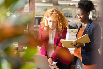 Dark-skinned assistant standing near boss using laptop