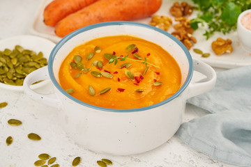 Carrot cream soup with pumpkin seeds and parsley and walnuts, side view on light background closeup