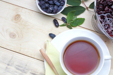 Fresh honeysuckle berries with jam, a cup of tea on a wooden table. Light rustic breakfast.
