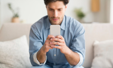 Serious Man Using Cellphone Sitting On Couch At Home