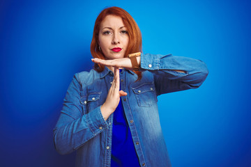 Young beautiful redhead woman wearing denim shirt standing over blue isolated background Doing time...