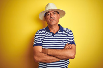 Handsome middle age man wearing striped polo and hat over isolated yellow background skeptic and nervous, disapproving expression on face with crossed arms. Negative person.