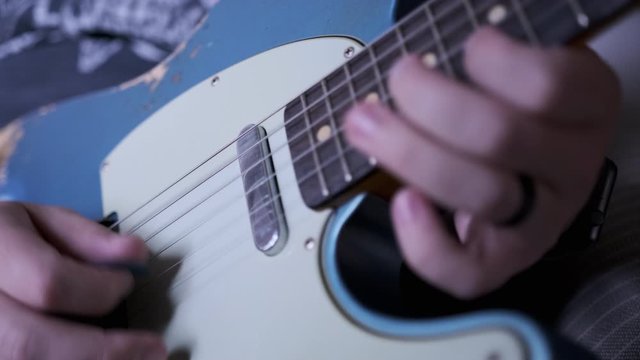 A man playing blue t-style guitar higher up the neck.