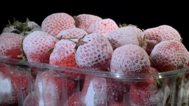 Fresh frozen strawberries in disposable plastic food pack on black background. Rotation 360 degrees, closeup