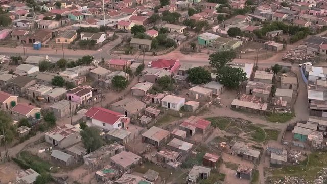 A township in South Africa with small low cost housing and informal shanty shack structures as a vehicle drives along the road.